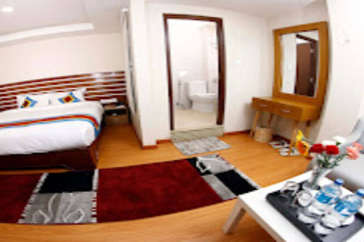 A hotel room with a bed, a desk with water bottles, a mirror, and a bathroom visible through an open door.