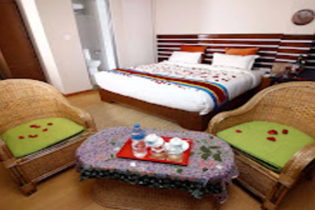 A hotel room with a bed, two wicker chairs, a small round table, and a wooden headboard.