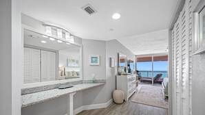 A modern bathroom with a large mirror, vanity, and a view of the ocean. - 🩱CBC 1-15E – Private balcony, beachfront, pool, gym & pickleball! (Clearwater)