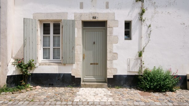 Un edificio con fachada de piedra, puerta verde y una pequeña ventana con contraventanas.