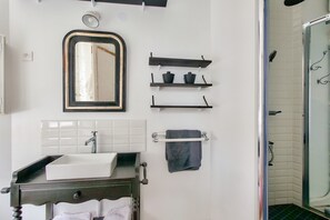 Ein Badezimmer mit einem weißen Waschbecken, einem Spiegel und zwei Regalen mit schwarzen Behältern.