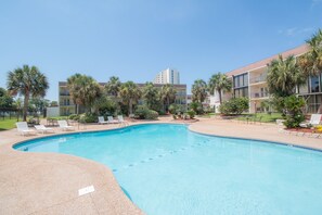 Ein Swimmingpool mit Liegestühlen, Palmen und ein Gebäude mit Balkonen im Hintergrund.