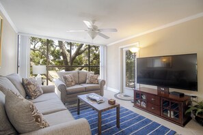 Ein Wohnzimmer mit einer Couch, einem Couchtisch, einem Fernseher auf einem Holzständer und einem Deckenventilator.