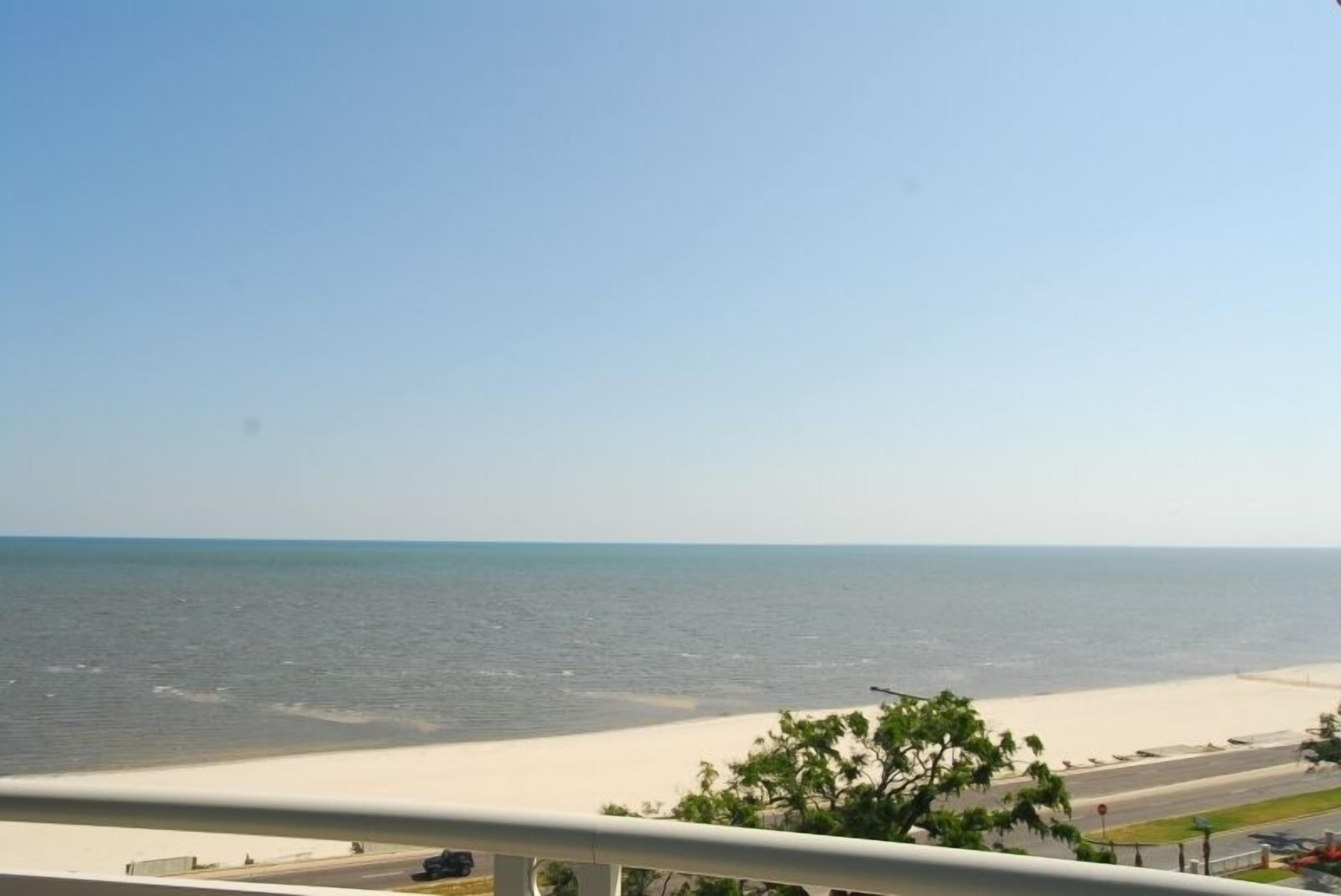 A view of a beach with a clear sky and a road in the foreground.