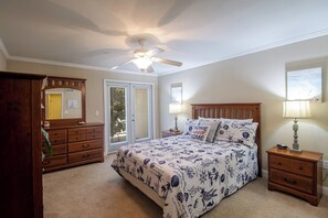 Ein Schlafzimmer mit einem Bett, einer Holzkommode, einem Nachttisch, einem Deckenventilator und einem Fenster mit Jalousien.