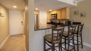 A kitchen with wooden cabinets, a microwave, a refrigerator, and a bar area with stools. - B.E.A.C.H.  Best Escape Anyone Could Have--  Let's Go!!  2 Bedroom / 2 Bath!! (Biloxi)