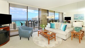 A spacious living room with a large window overlooking the ocean, a flat-screen TV, a sofa with decorative pillows, and a coffee table. - Gorgeous Waikiki Ocean View! Full Kitchen, Free Wi-Fi, Close to Beach! (Honolulu)