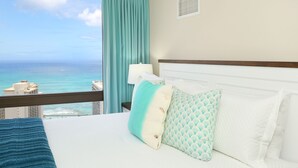 A hotel room with a bed, a nightstand, a lamp, and a view of the ocean. - Gorgeous Waikiki Ocean View! Full Kitchen, Free Wi-Fi, Close to Beach! (Honolulu)