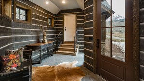 A log cabin interior with a staircase leading to a door, a wooden bench with a deer head sculpture, and a fur rug on the floor. - New Luxury home in Cascade Village - 2 miles to Purgatory - AC - Hot Tub/Pool (Durango)