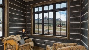 A log cabin interior with a large window offering a mountain view, a wooden chair, and a patterned sofa. - New Luxury home in Cascade Village - 2 miles to Purgatory - AC - Hot Tub/Pool (Durango)