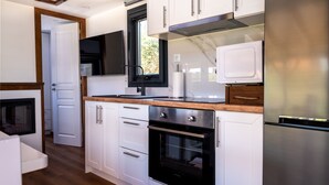 A compact kitchen with white cabinets, a built-in oven, a microwave, and a stainless steel refrigerator. - Tiny Villa among the Olives. (hERAKLION)