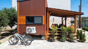 A modern, compact building with a stone facade, a wooden deck, and a bicycle parked outside. - Tiny Villa among the Olives. (hERAKLION)