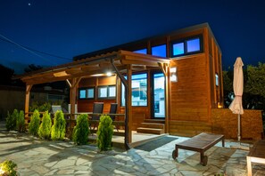 Een modern houten huis met een overdekt terras, buitenmeubels en een terras met stenen tegels.