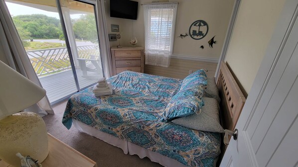 A bedroom with a bed, a nightstand, a TV, and a balcony with a view of greenery.