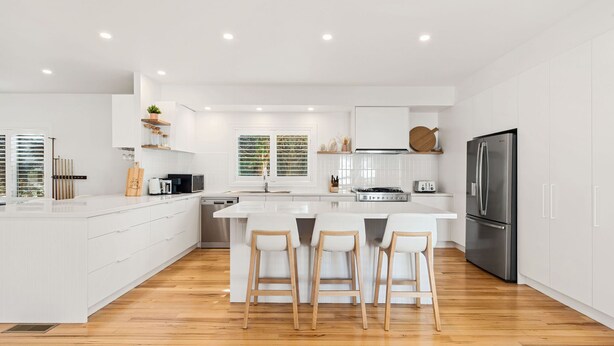 A modern kitchen with white cabinetry, a large island with bar stools, a stainless steel refrigerator, and wooden flooring. - Ultimate family retreat, on the Portsea / Sorrento border, (sleeps 15/16) (Portsea)