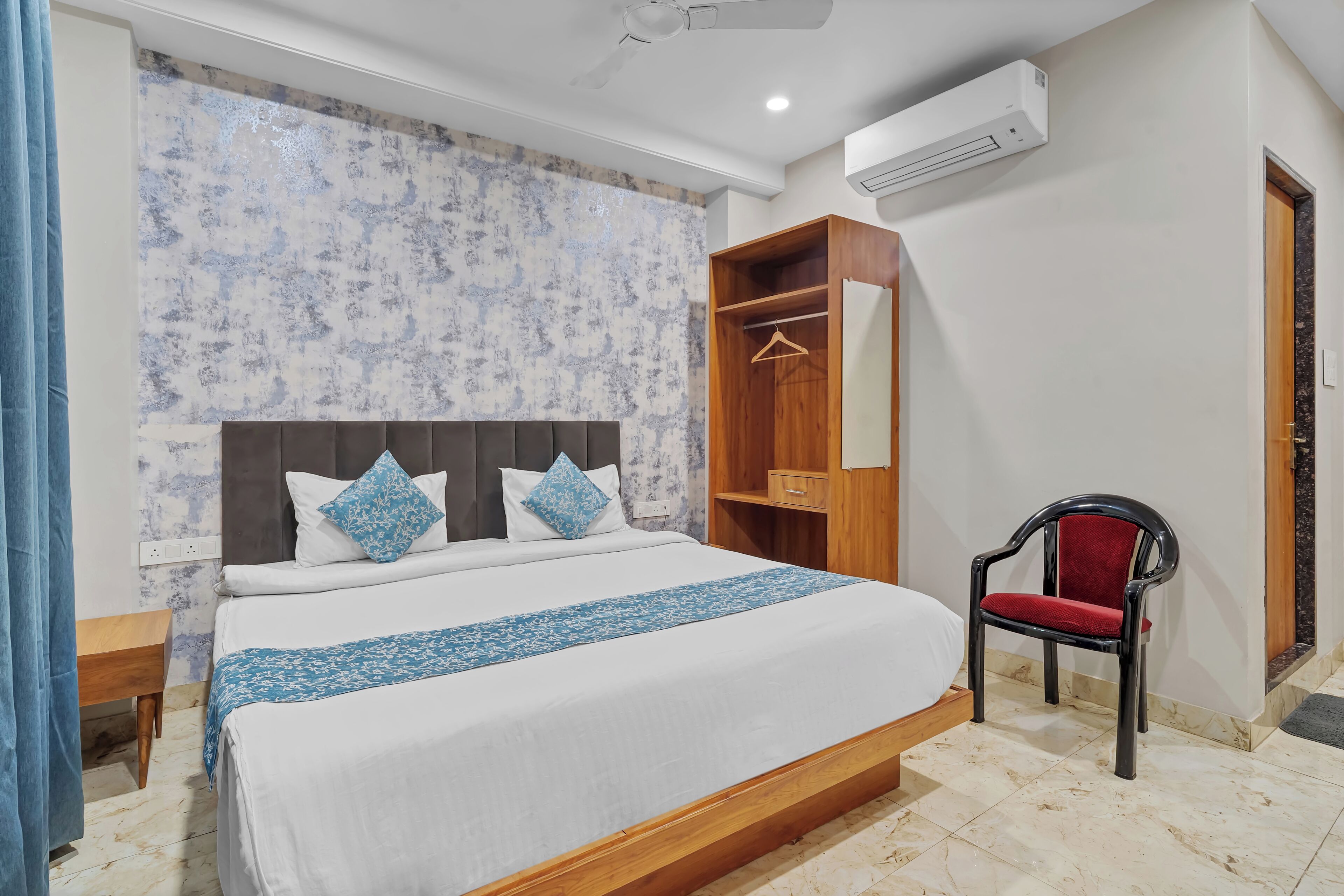 A neatly arranged bedroom with a bed, a wooden wardrobe, a chair, and an air conditioning unit.