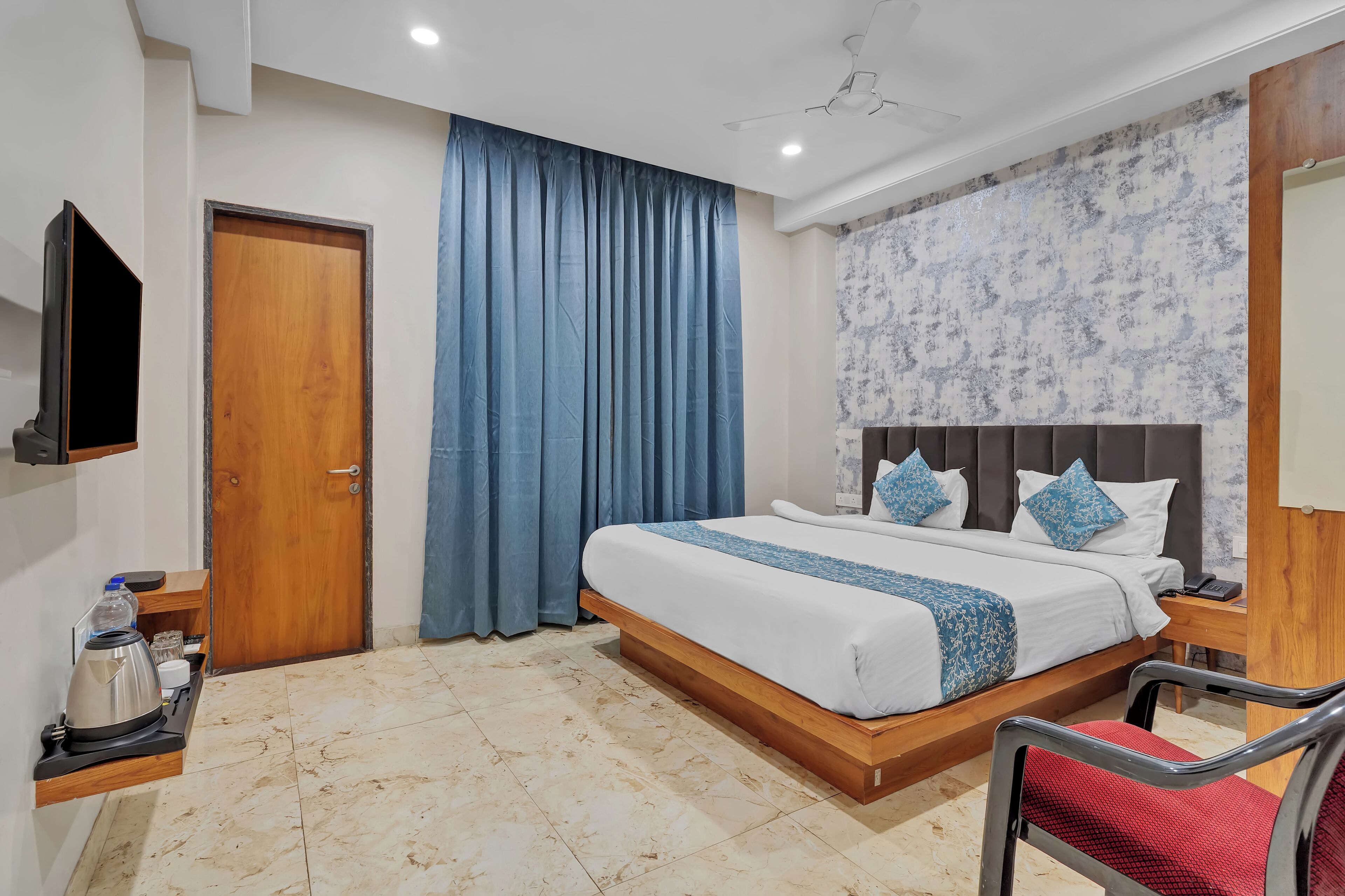A hotel room with a wooden bed, a flat-screen TV, a coffee maker, and a red chair.