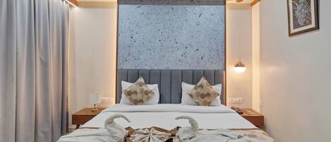 A hotel room with a large bed, a headboard with a textured panel, two bedside lamps, and a framed picture on the wall.