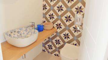 Ein Badezimmer mit Waschbecken, Holzablage, Wand mit Fliesenmuster und Toilette.