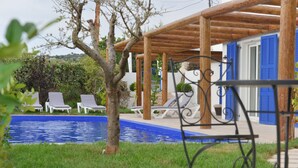 Ein Poolbereich mit Liegestühlen, einer Pergola und einem Gebäude mit blauen Fensterläden.