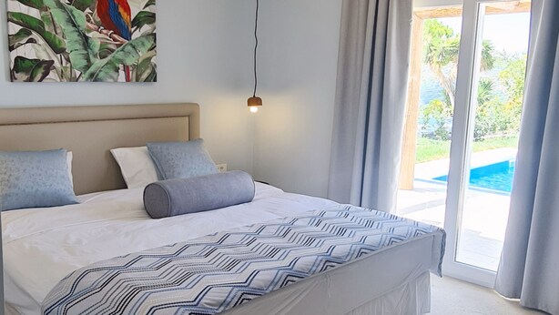 Ein Schlafzimmer mit einem Bett, einem Papageienbild, einer Deckenleuchte und Blick auf einen Pool durch eine Glastür.