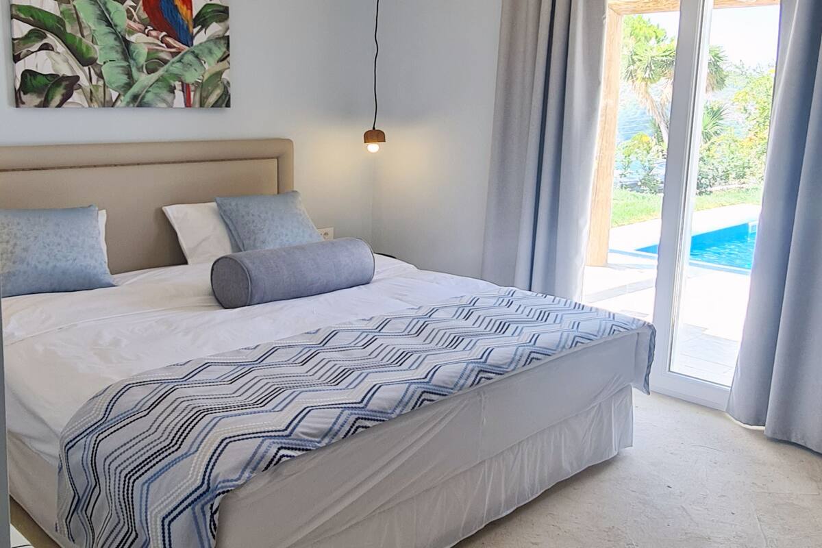 A bedroom with a bed, a painting of a parrot, a ceiling light, and a view of a pool through a glass door.