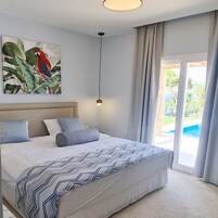 Un dormitorio con una cama, un cuadro de un loro, una lámpara en el techo y vistas a una piscina a través de un vidrio.