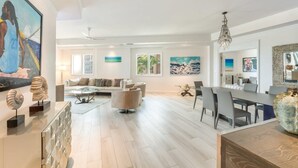 Ein geräumiges Wohnzimmer mit einer modernen Couch, einem Essbereich mit einem langen Tisch und einer Küche im Hintergrund.