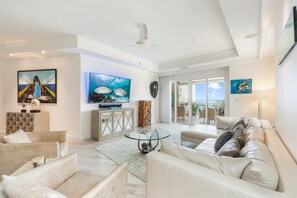 A spacious living room with a large TV, comfortable seating, and a view of the outdoors. - Luxury Three Bedroom Oasis (Seven Mile Beach)