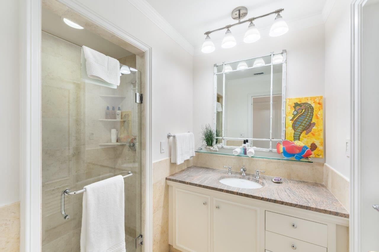 A modern bathroom with a glass shower enclosure, a vanity with a sink and mirror, and a colorful artwork on the wall.