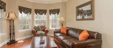 A living room with a brown leather sofa, a wooden coffee table, a floor lamp, and a painting on the wall.