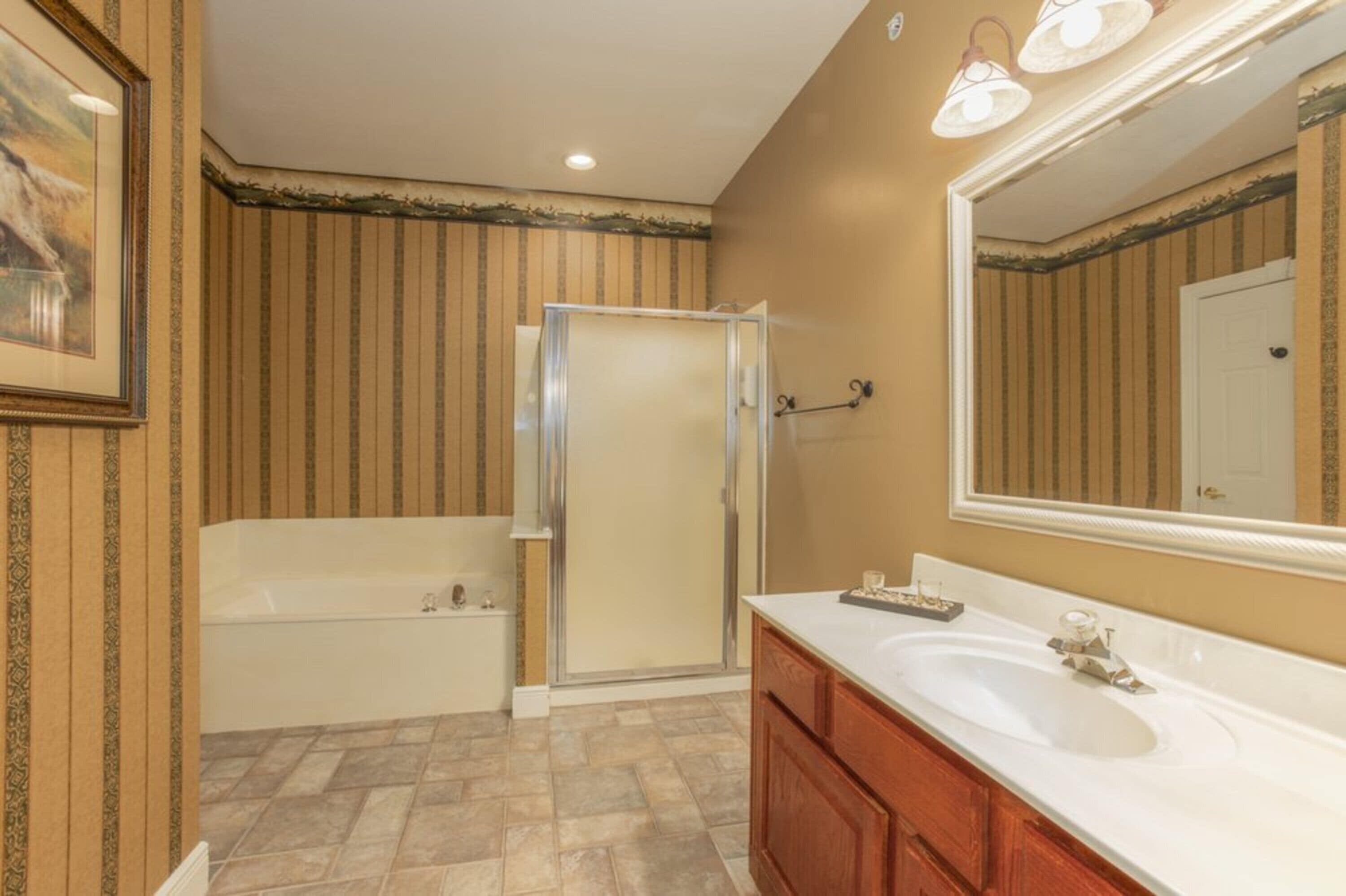 A bathroom with a bathtub, a shower enclosure, a sink, and a large mirror.