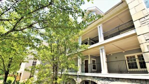 Un edificio de dos pisos con un balcón en el nivel superior, arcos de piedra en la planta baja y un patio arbolado.