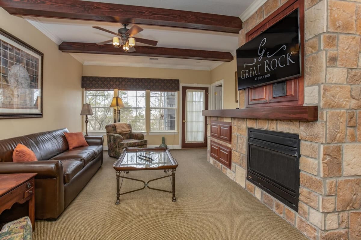 A cozy living room with a stone fireplace, leather sofa, and a coffee table.