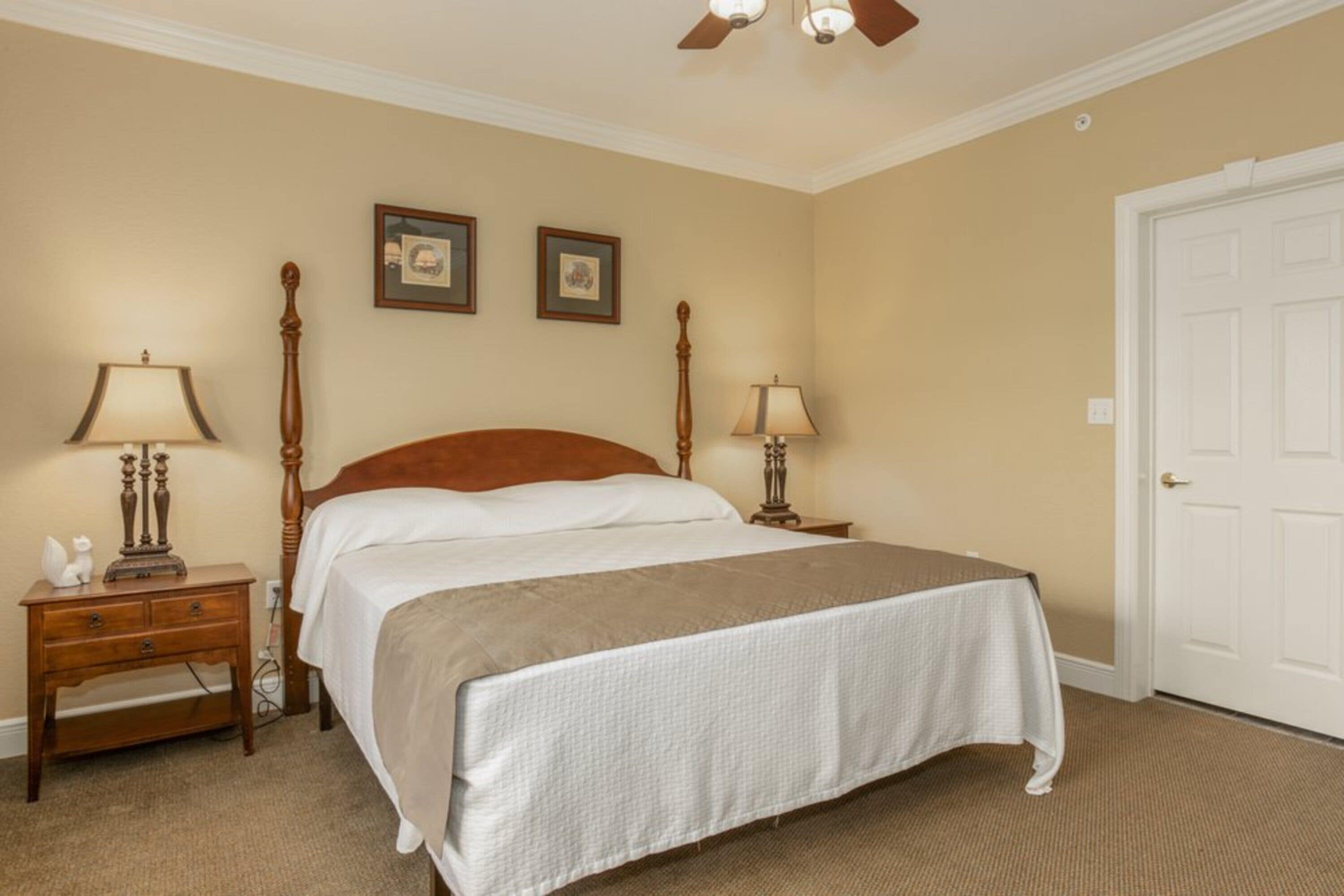 A bedroom with a large bed, two bedside tables with lamps, a door, and two framed pictures on the wall.