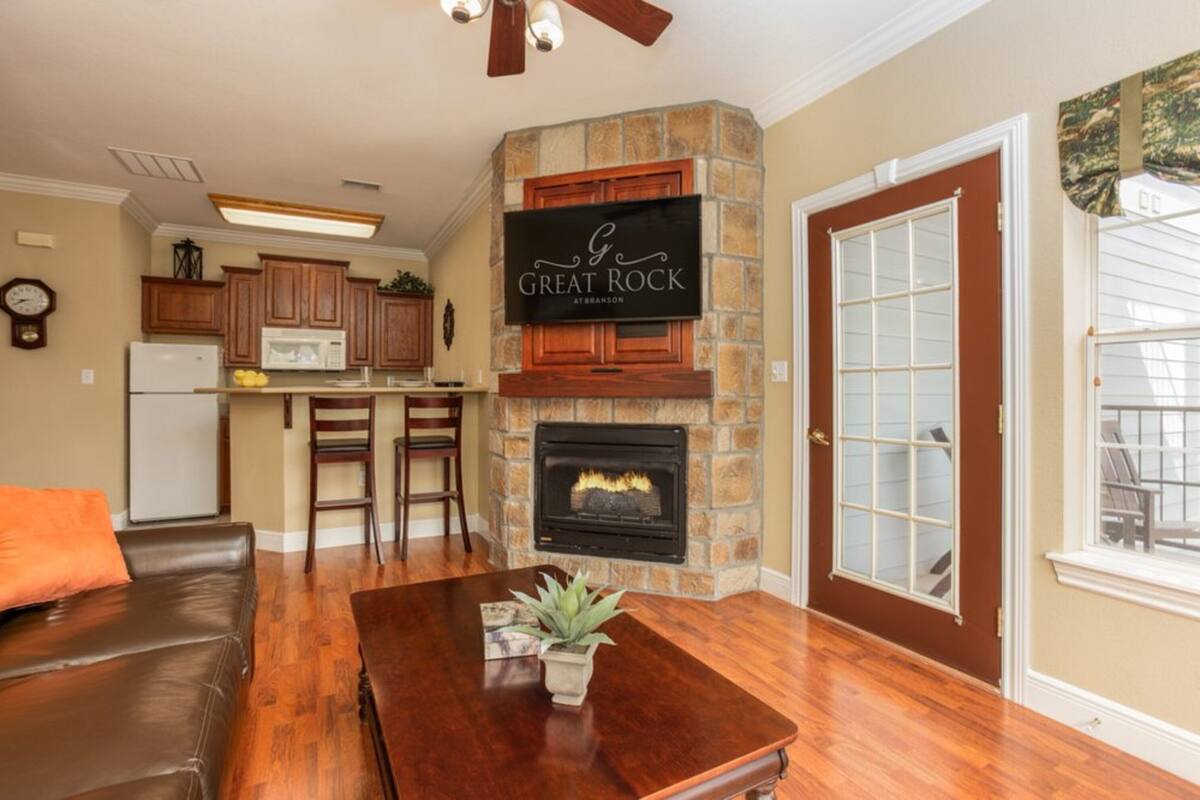 A living room with a fireplace, wooden cabinets, a dining table, and a kitchen in the background.