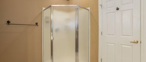 A corner bathroom with a glass shower enclosure, a white door, and beige walls.