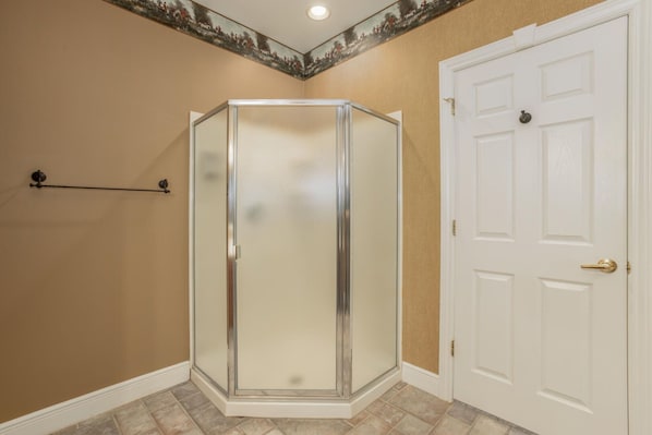 A corner bathroom with a glass shower enclosure, a white door, and beige walls.