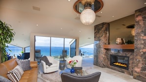 A modern living room with a leather sofa, a glass coffee table, and a fireplace. - Enchanting Oasis Stunning Luxury Oceanfront Condo -180° Ocean Views + Pool (Solana Beach)
