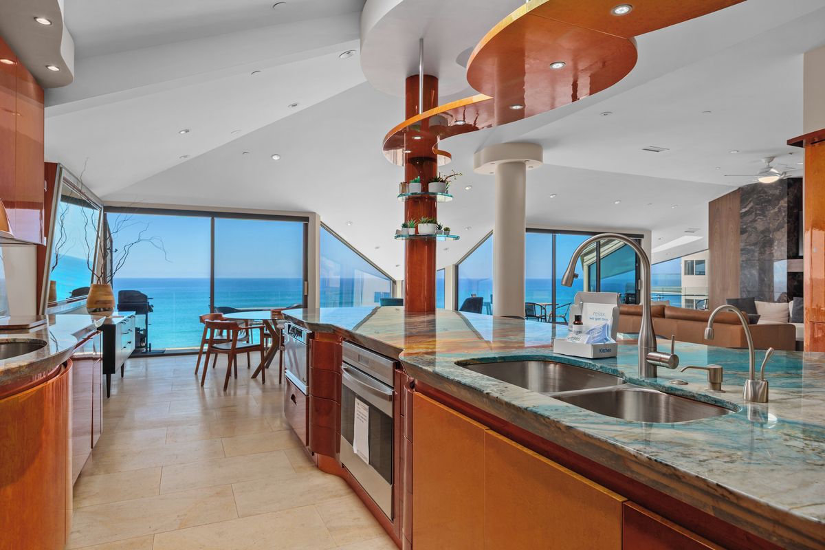 A modern kitchen with a large island, a dining area with a view of the sea, and a living space with a sofa and a coffee table.