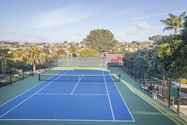Una cancha de tenis con una red, rodeada por una cerca y árboles.