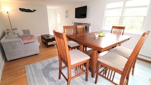 A dining area with a wooden table and chairs, a grey sofa, and a fireplace. - Great Home in a Quiet Neighborhood Yet Close to Town and Beaches (2312) (Dennis)