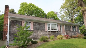 A single-story house with a brick chimney, shingled exterior, and a front porch. - Great Home in a Quiet Neighborhood Yet Close to Town and Beaches (2312) (Dennis)