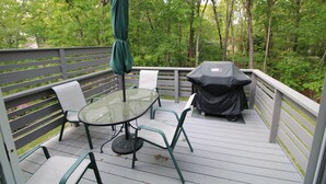 A deck with a glass table and chairs, a green umbrella, and a barbecue grill. - Great Home in a Quiet Neighborhood Yet Close to Town and Beaches (2312) (Dennis)