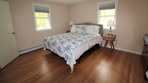 A bedroom with a bed, two bedside tables, a nightstand, a ceiling fan, and two windows with blinds. - Great Home in a Quiet Neighborhood Yet Close to Town and Beaches (2312) (Dennis)
