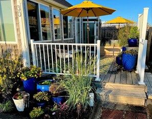 A wooden deck with a white railing, surrounded by potted plants and a yellow umbrella.