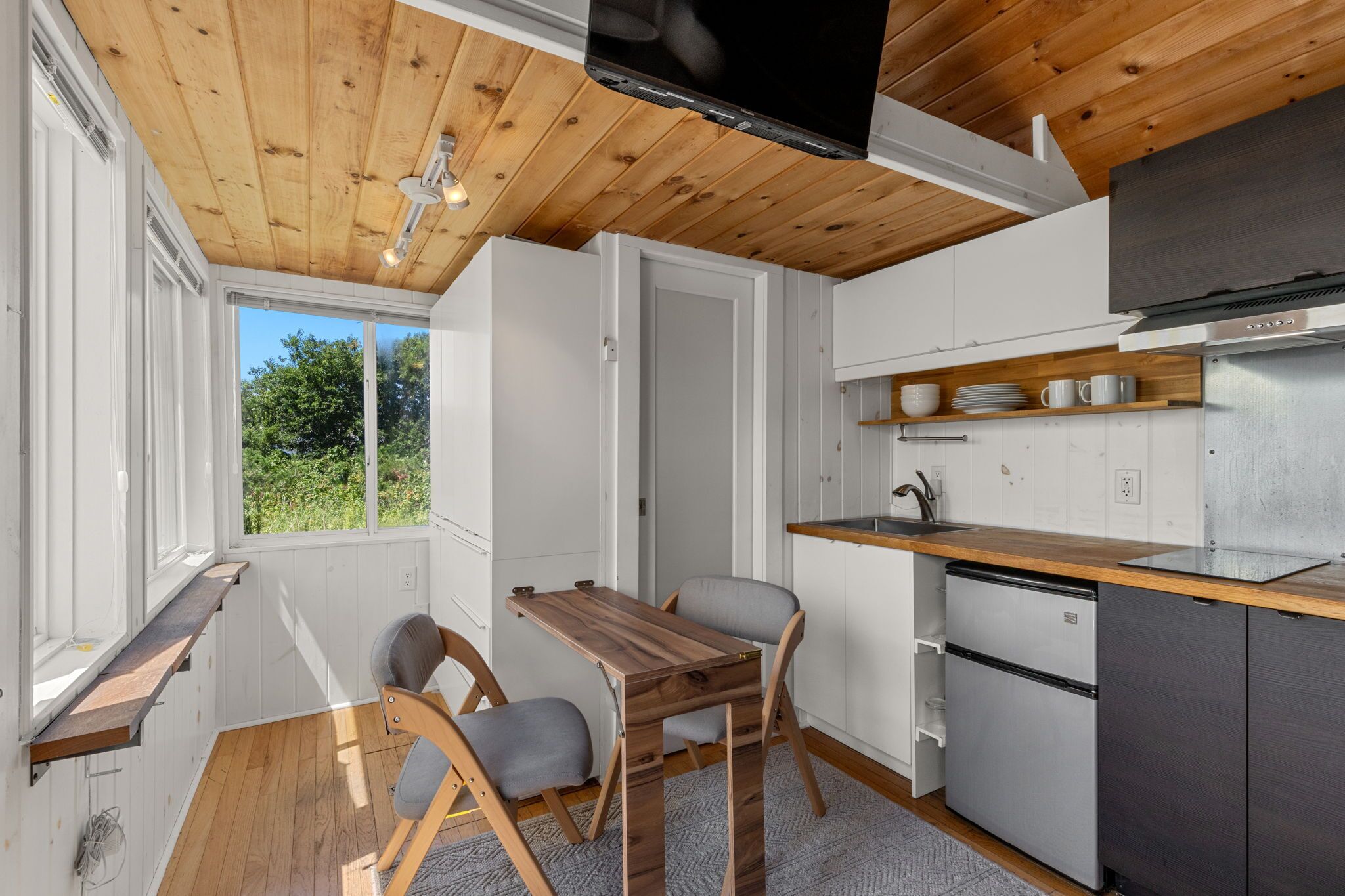 A compact kitchen with a wooden ceiling, a built-in TV, and a small dining area with a table and chairs.