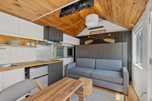 A compact kitchen with modern appliances, a grey sofa, and a wooden dining table.