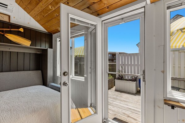 A room with a bed, a wooden ceiling, and a sliding glass door leading to an outdoor deck. - Cozy Bayside Cottage With Huge Outdoor Living Space and Private Beach (2313) (Provincetown)