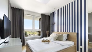 A modern hotel room with a large bed, a flat-screen TV, a glass desk, and a window with curtains. - Elite Apartments Seastory (Gdansk)